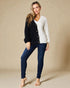 Woman wearing a black cardigan over a white shirt with blue jeans on a beige background