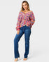 Woman wearing a colorful off-shoulder sweater and blue jeans on a white background