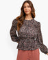 A woman modeling a long-sleeve peplum blouse with an intricate abstract pattern in black, pink, and white, paired with dusty rose pleated pants against a clean white background.
