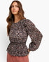 A woman modeling a long-sleeve blouse with a black, pink, and white floral paisley pattern and a smocked waist, paired with a dusty rose skirt against a plain white background.