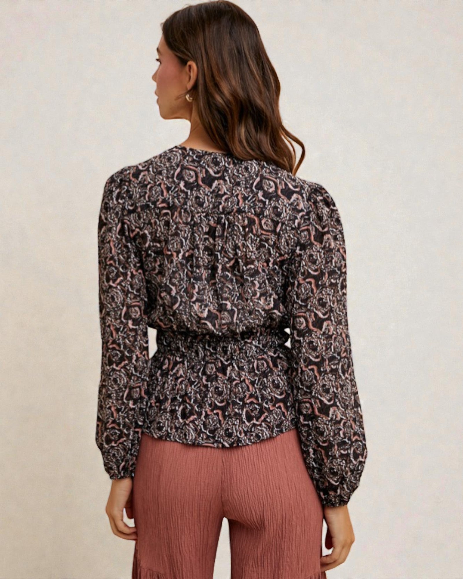 Woman wearing a patterned blouse and pink pants against a neutral background