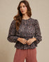 Woman wearing a patterned blouse and pink pants against a beige background