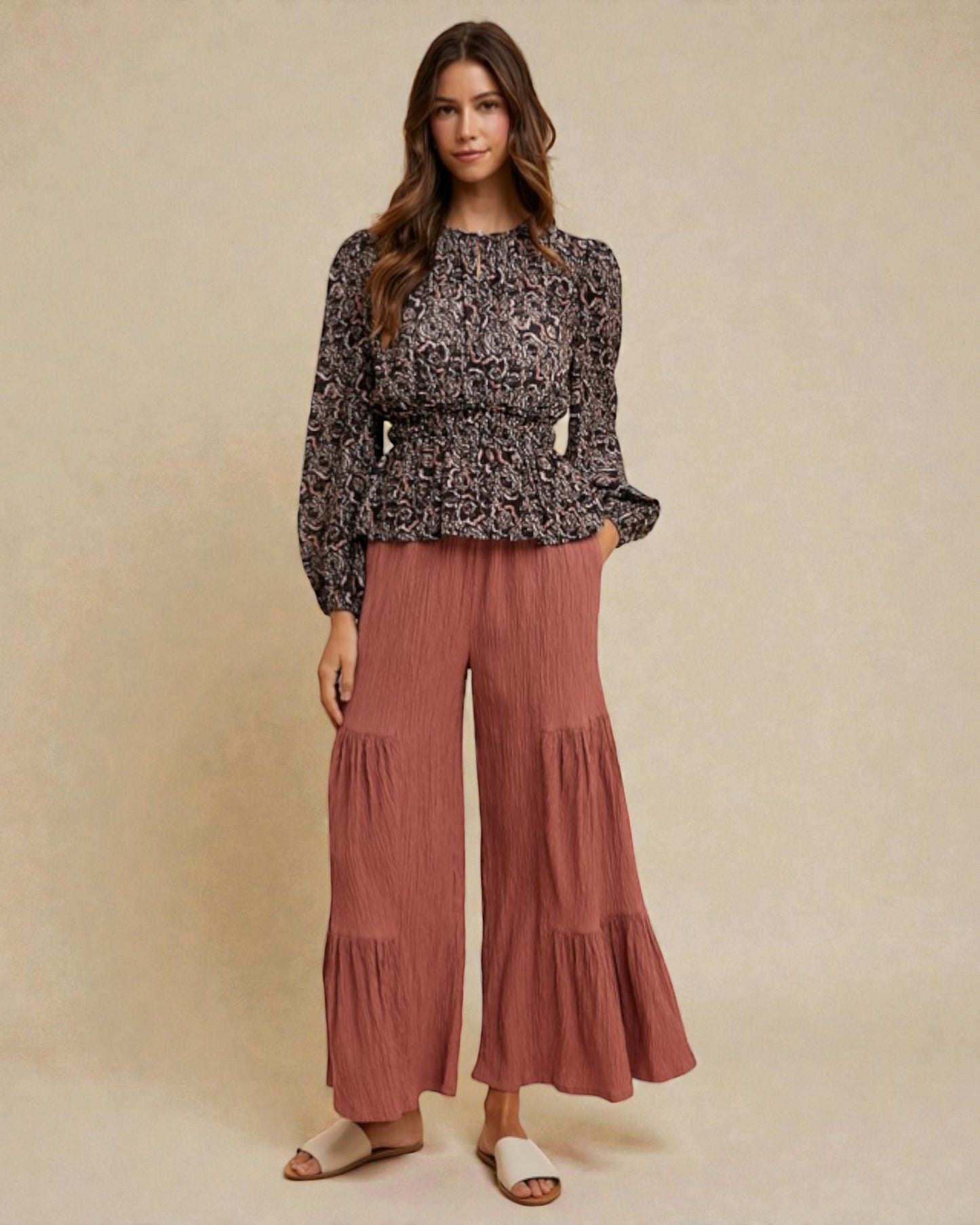 Woman wearing a patterned top and wide-leg pants on a beige background