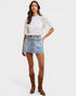 Woman wearing a white blouse with lace details, denim skirt, and brown boots on a white background