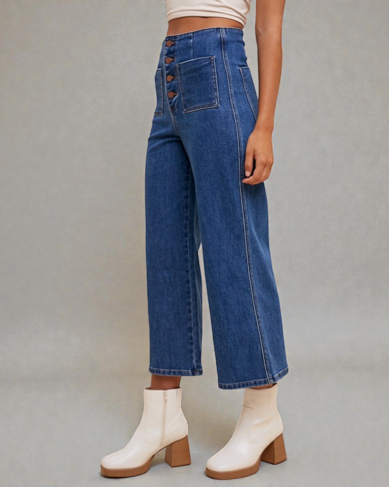 Person wearing blue jeans and white boots on a plain background
