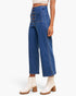 A model wearing high-waisted, wide-leg blue denim jeans with a button-fly front and decorative front pockets, paired with cream ankle boots, against a plain white studio background.