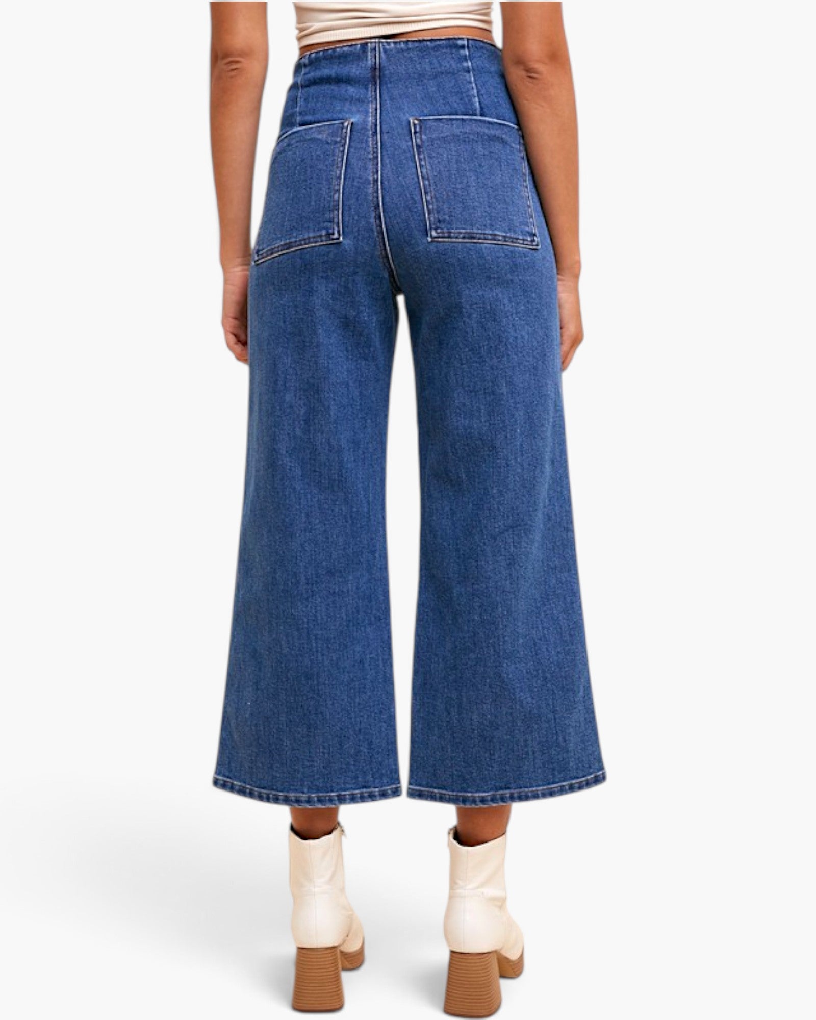 A model shown from the back wearing blue wide-leg cropped jeans, cream ankle boots, and a beige crop top against a light gray studio background.