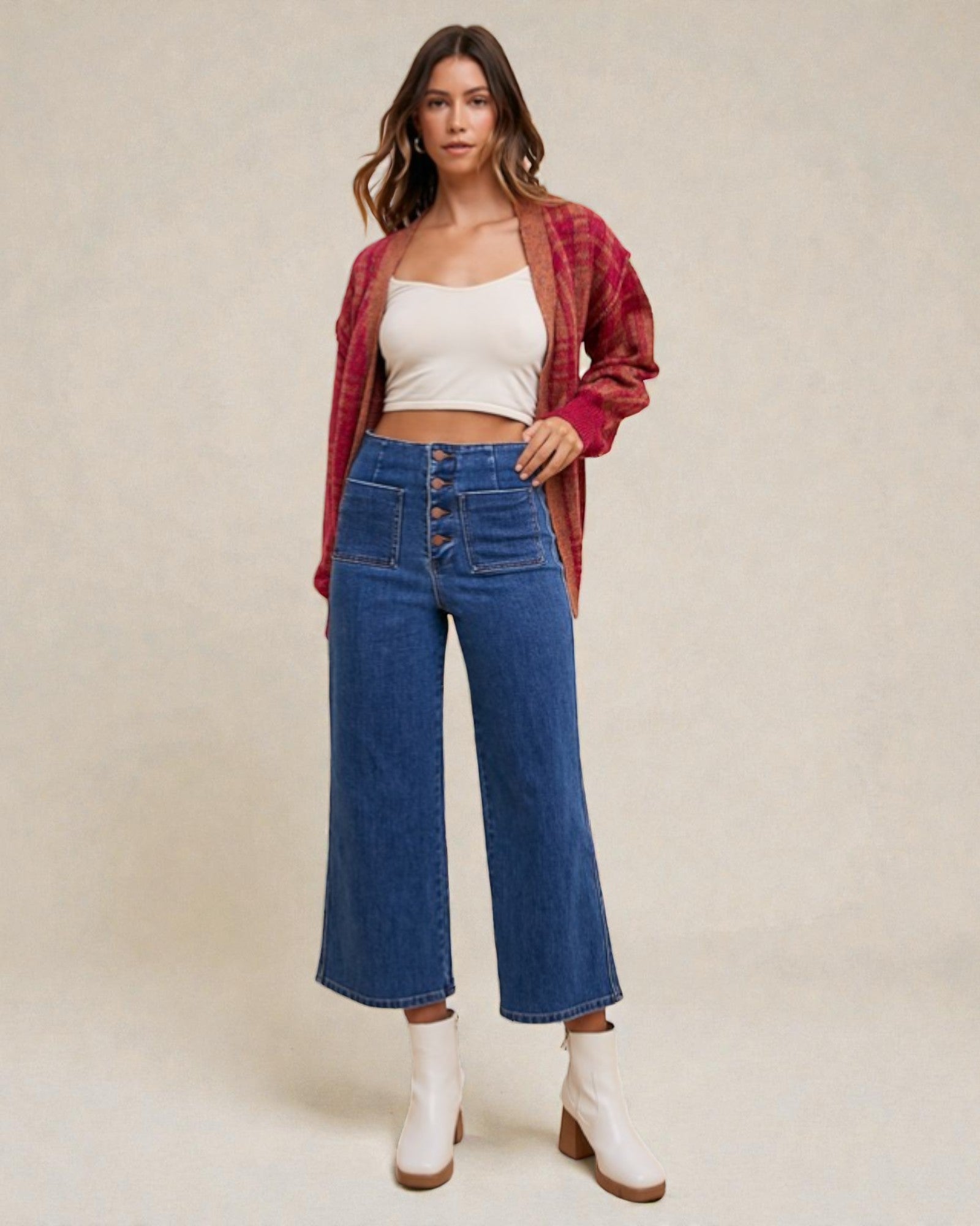 Woman wearing a white top, red plaid cardigan, blue jeans, and white boots on a beige background