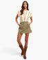 A woman modeling a short-sleeve knit top with cream, pink, and sage green stripes, paired with an olive green mini skirt and brown cowboy boots, against a light gray studio background.