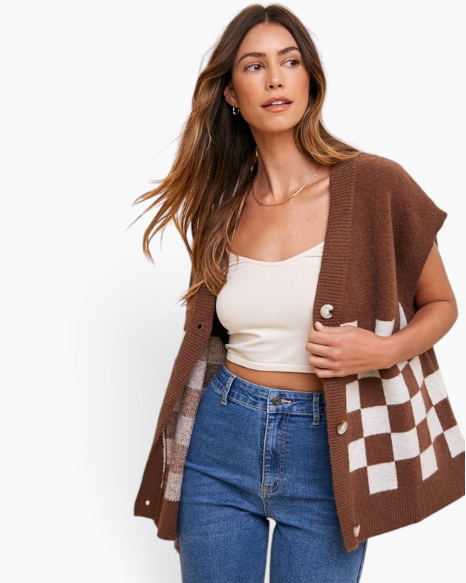 A woman modeling a brown knit cardigan with a brown and white checkerboard pattern on the front, worn open over a cream camisole and blue jeans against a plain white background.