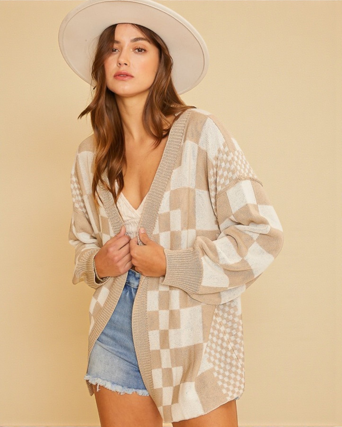 Woman wearing a patterned cardigan and denim shorts against a beige background