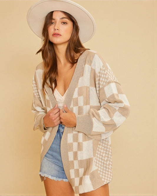 Woman wearing a patterned cardigan and denim shorts against a beige background