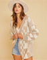 Woman wearing a patterned cardigan and denim shorts against a beige background
