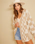 Woman wearing a checkered cardigan, denim shorts, and a white hat against a beige background