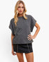A blonde model wearing a black and white checkerboard short-sleeve top and a black denim mini skirt with silver studs, posed against a solid white studio background.