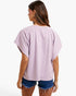 A woman shown from the back wearing a lavender and white checkerboard patterned short-sleeve top with denim shorts against a plain white background.