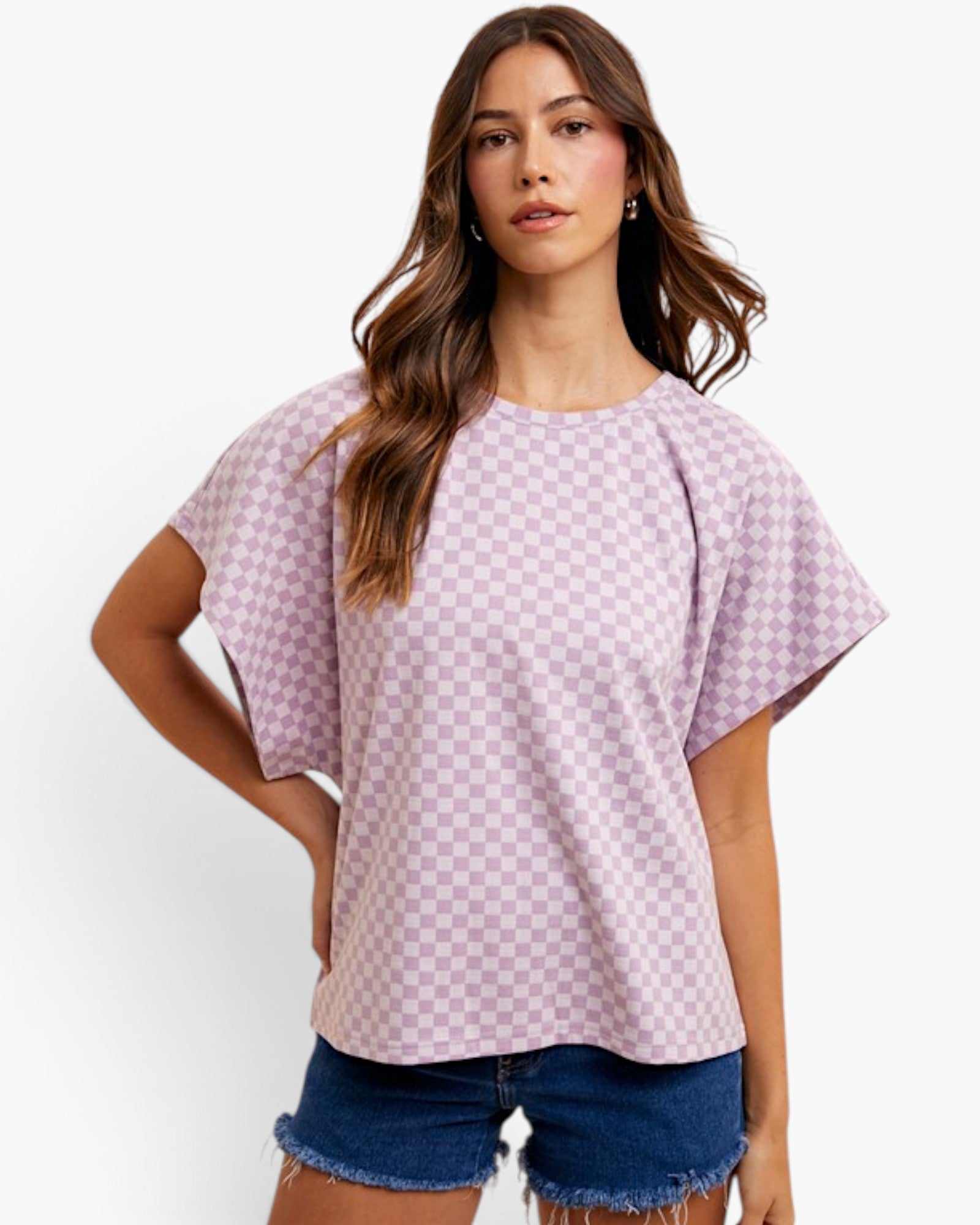 A woman modeling a lavender and white checkerboard short-sleeve top with a relaxed fit, paired with denim shorts, against a plain white background.