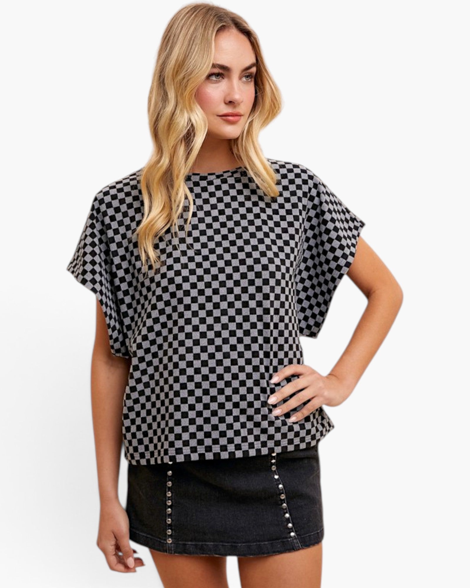 A woman modeling a black and white checkerboard short-sleeve top with a relaxed fit, paired with a dark denim skirt, against a plain white studio background.