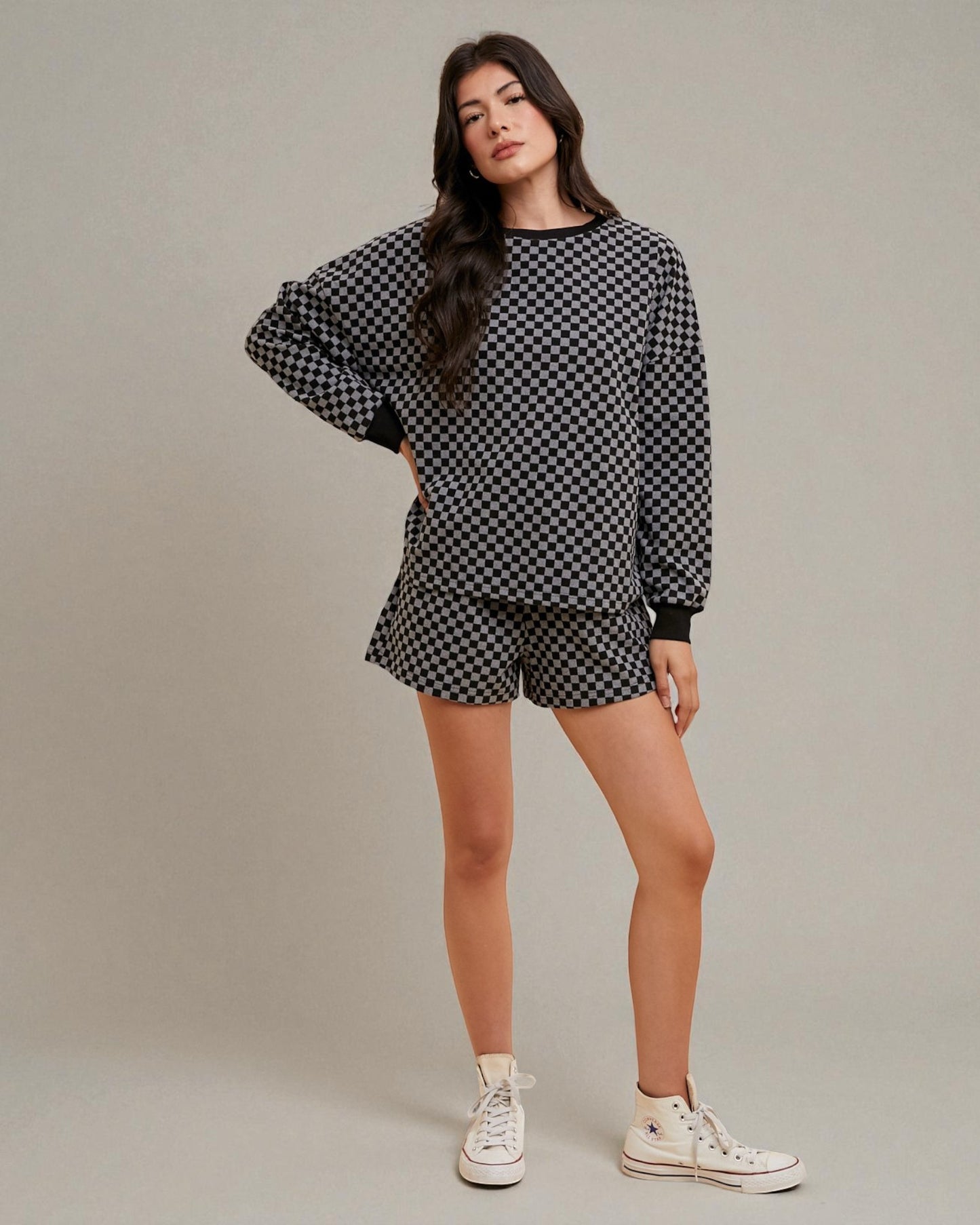 Woman wearing a black and white checkered outfit with white sneakers on a plain background