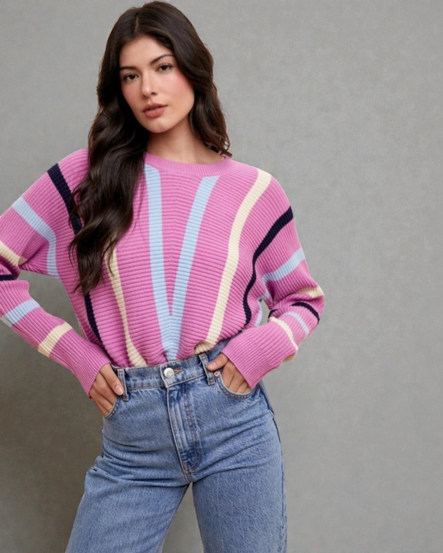 Woman wearing a colorful striped sweater and blue jeans against a gray background