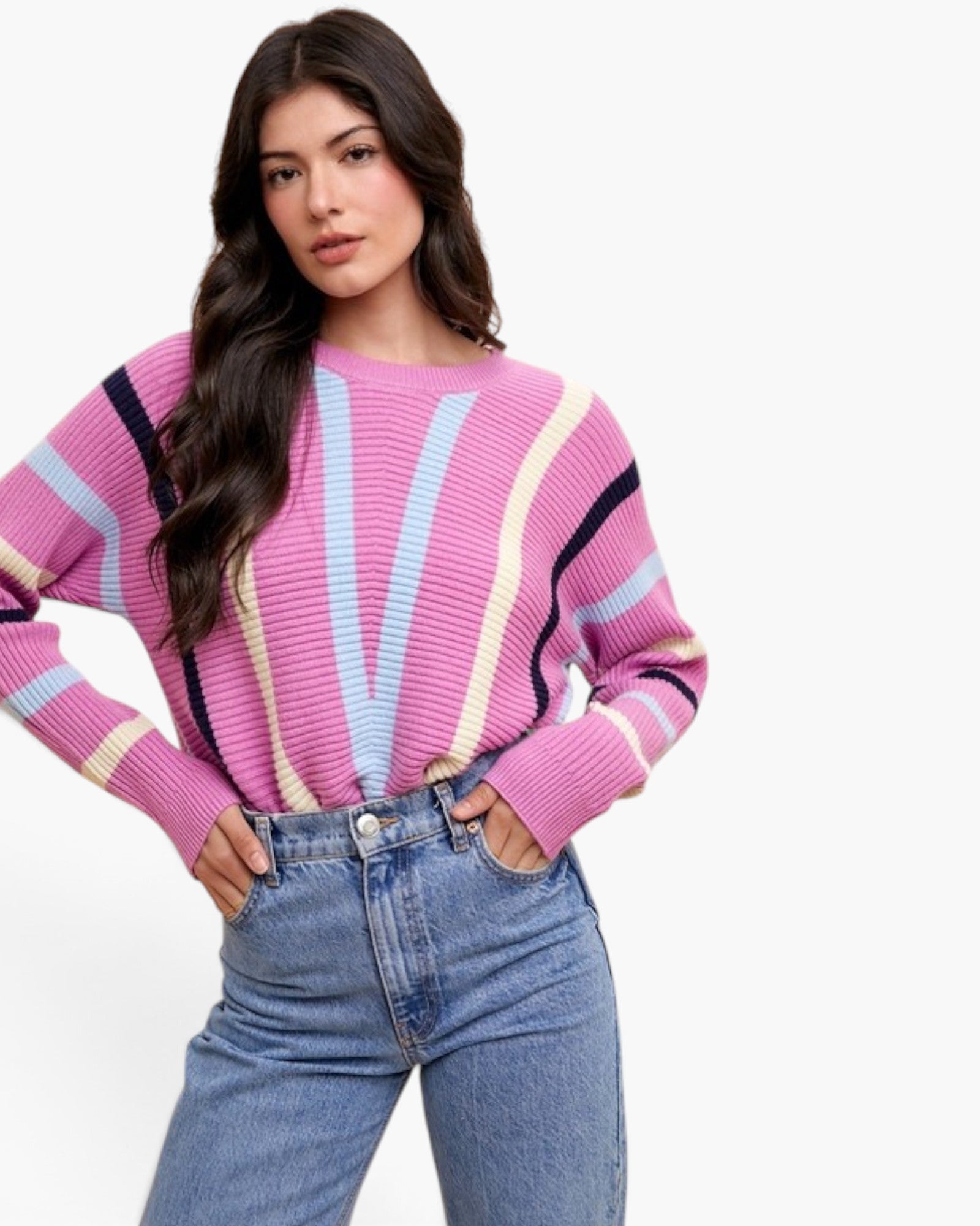 A woman modeling a pink ribbed knit sweater with vertical stripes in light blue, pale yellow, and black, paired with blue jeans against a plain white background.