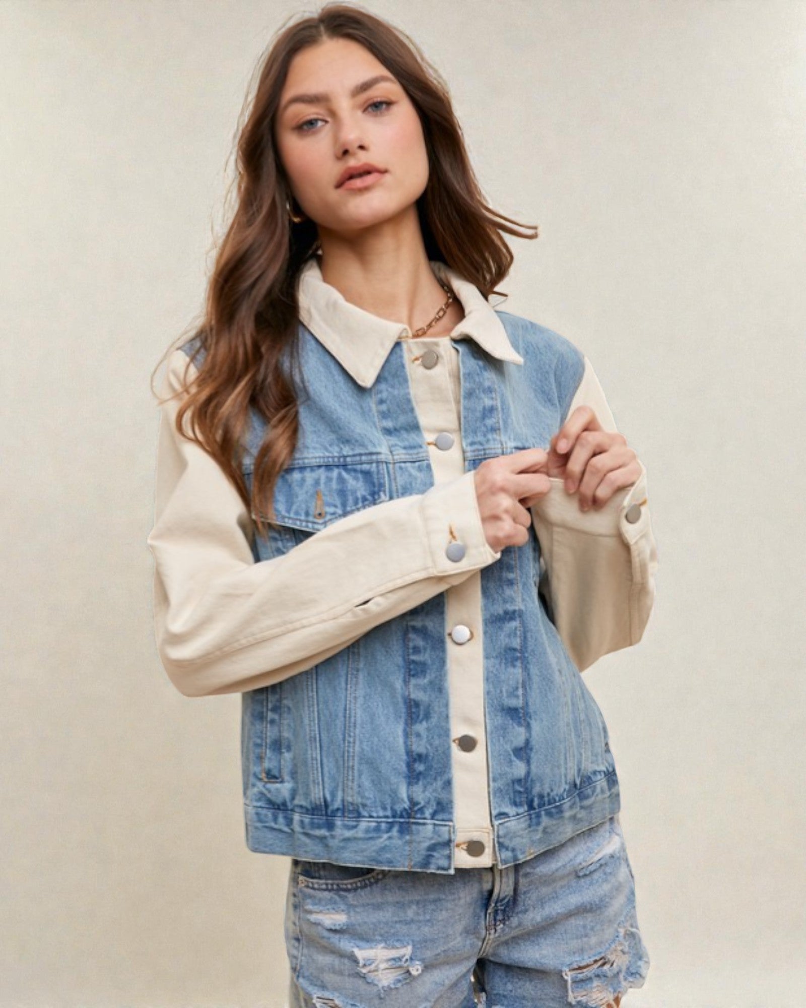 Woman wearing a denim jacket with beige collar and cuffs on a plain background