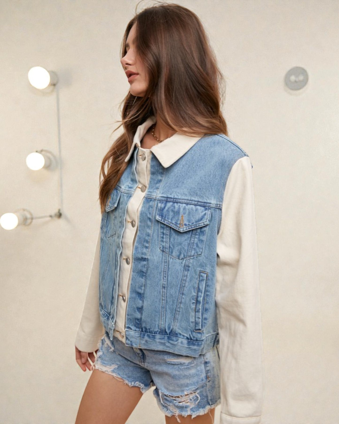Woman wearing a denim vest over a white shirt with a plain background