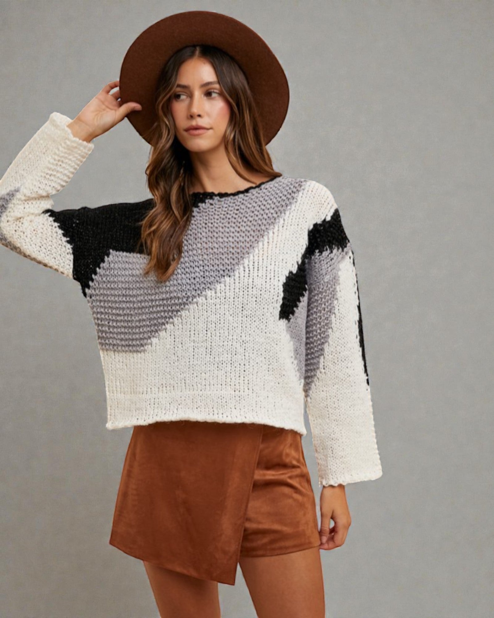 Woman wearing a patterned sweater and brown shorts against a gray background