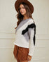 Woman wearing a patterned sweater and brown hat against a white wall