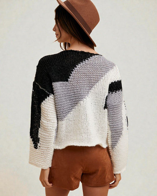 Person wearing a black, gray, and white patterned sweater with brown shorts and hat on a light background