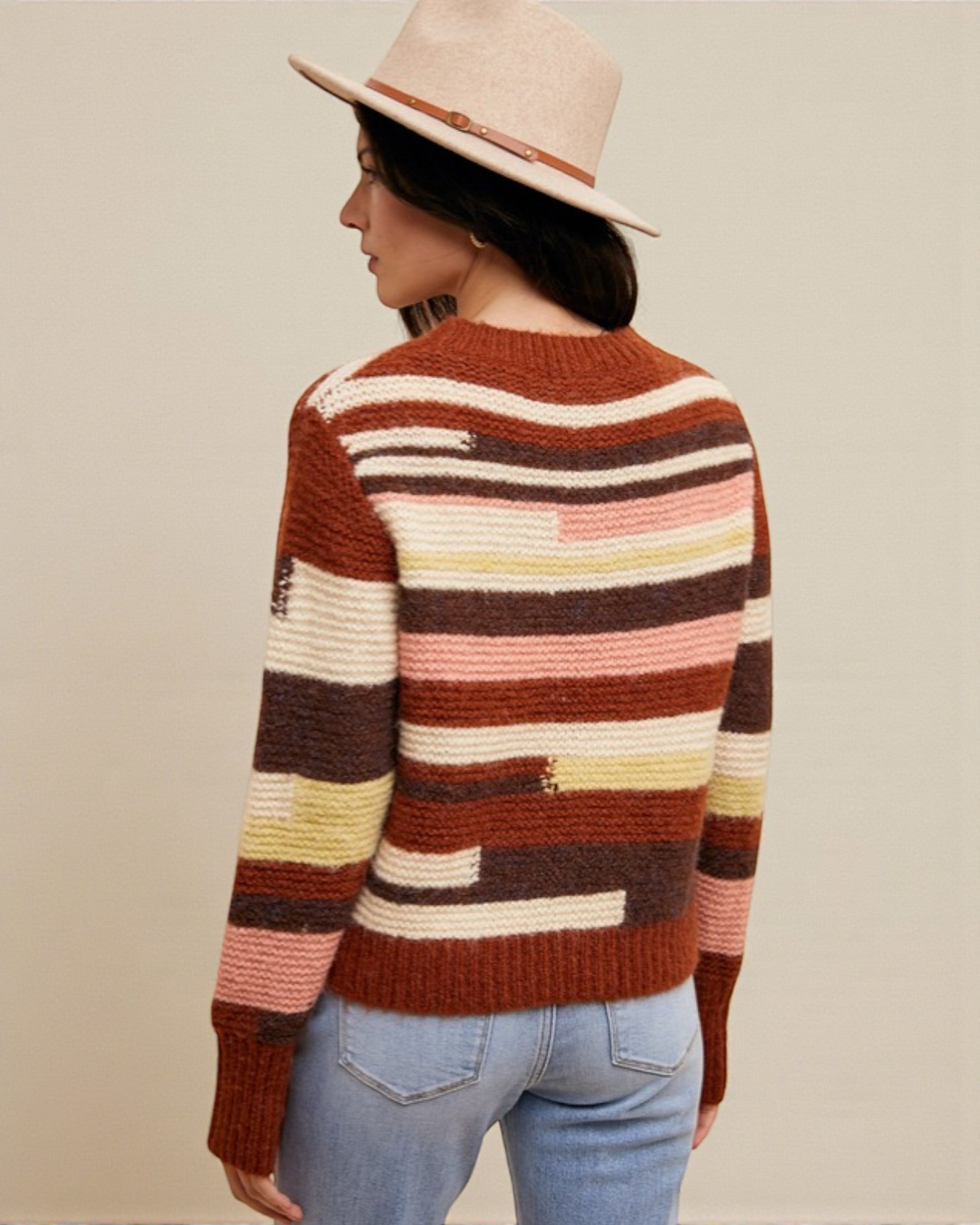 Person wearing a colorful striped sweater and hat on a beige background