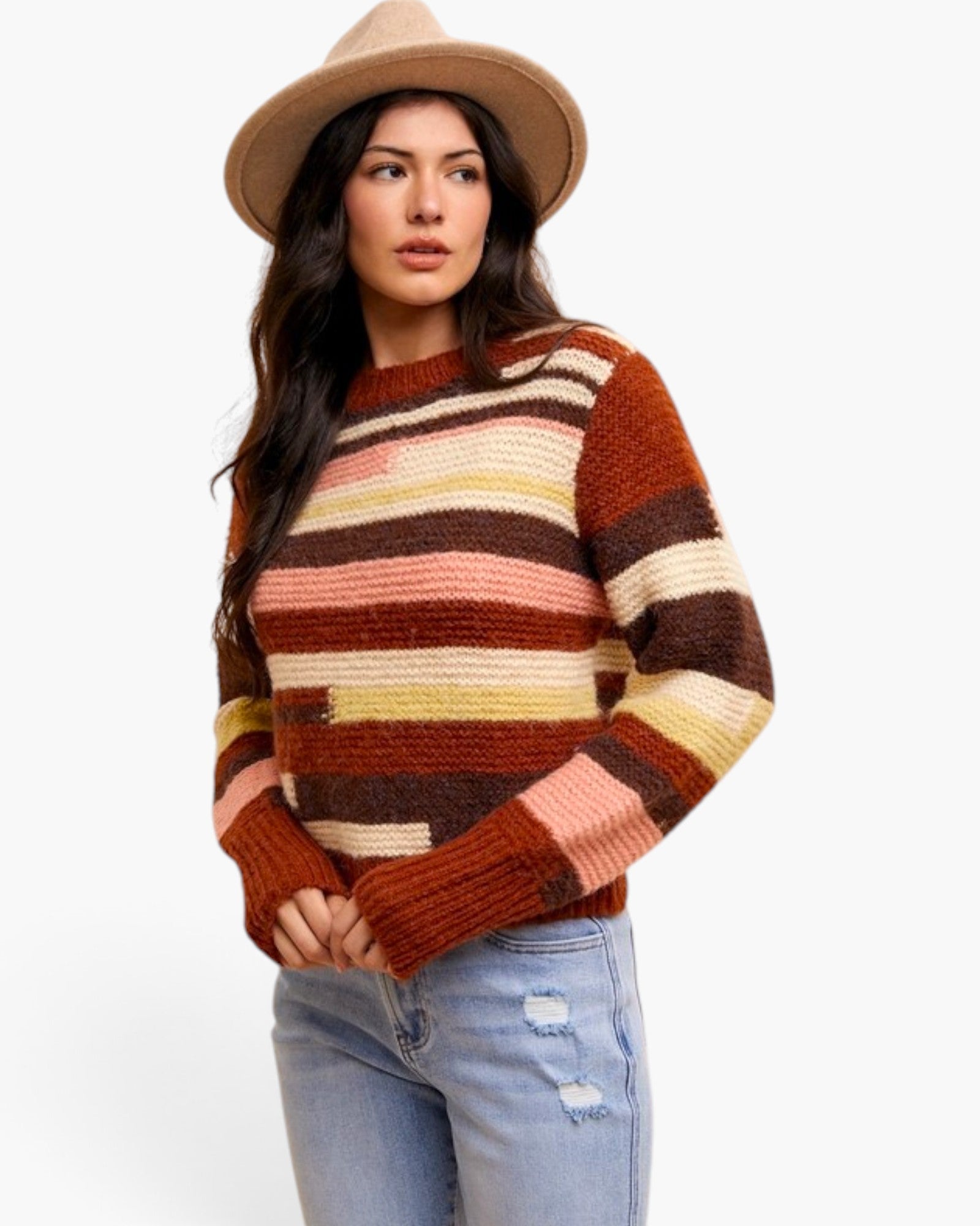 A woman wearing a chunky knit sweater with horizontal stripes in rust orange, brown, cream, and dusty pink, paired with light blue jeans and a tan wide-brim hat, against a plain white background.