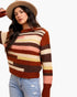 A woman wearing a brown, rust, and cream striped knit sweater, a beige wide-brim hat, and light-wash distressed jeans, photographed against a plain white background.
