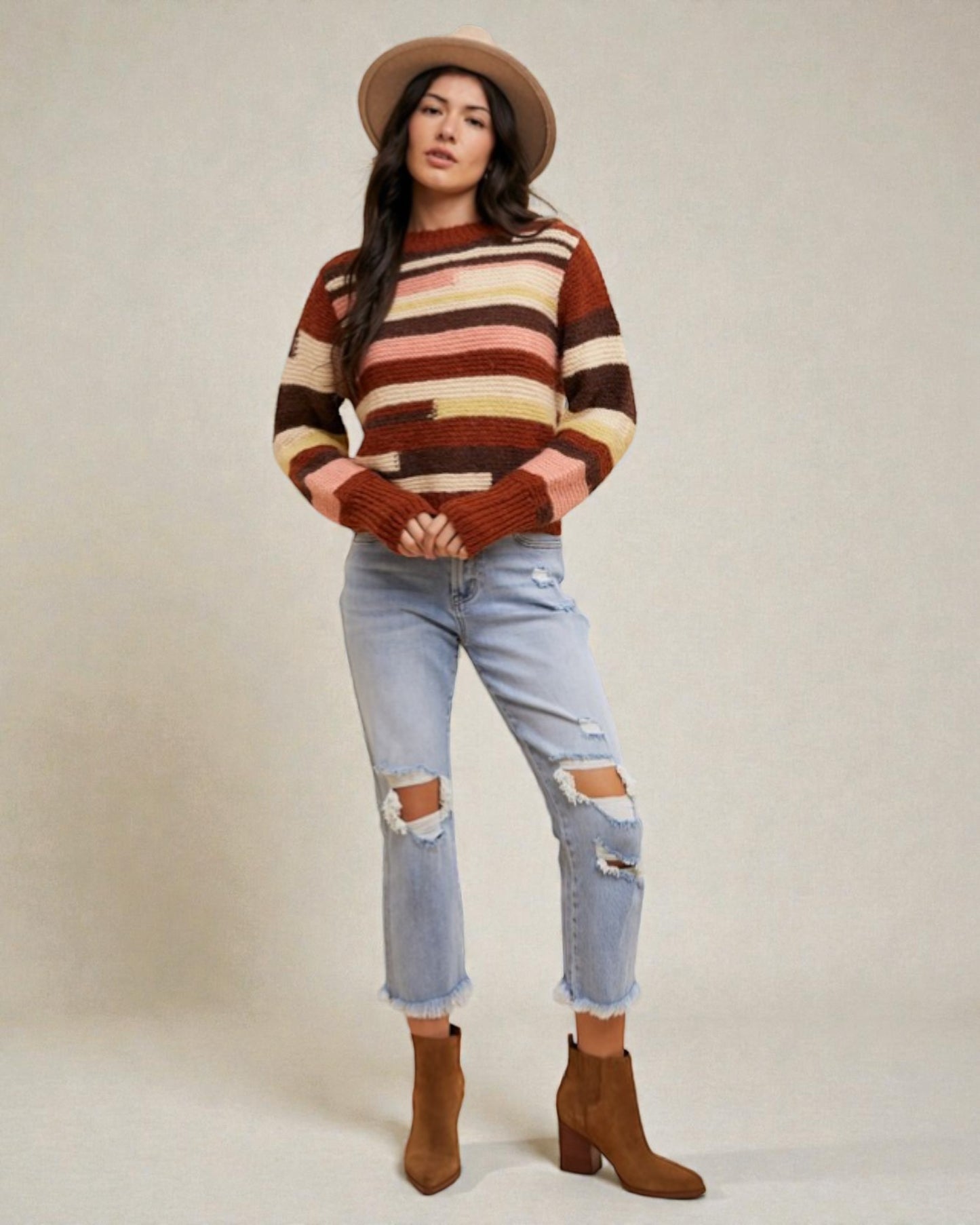 Woman wearing a striped sweater, jeans, and boots on a plain background