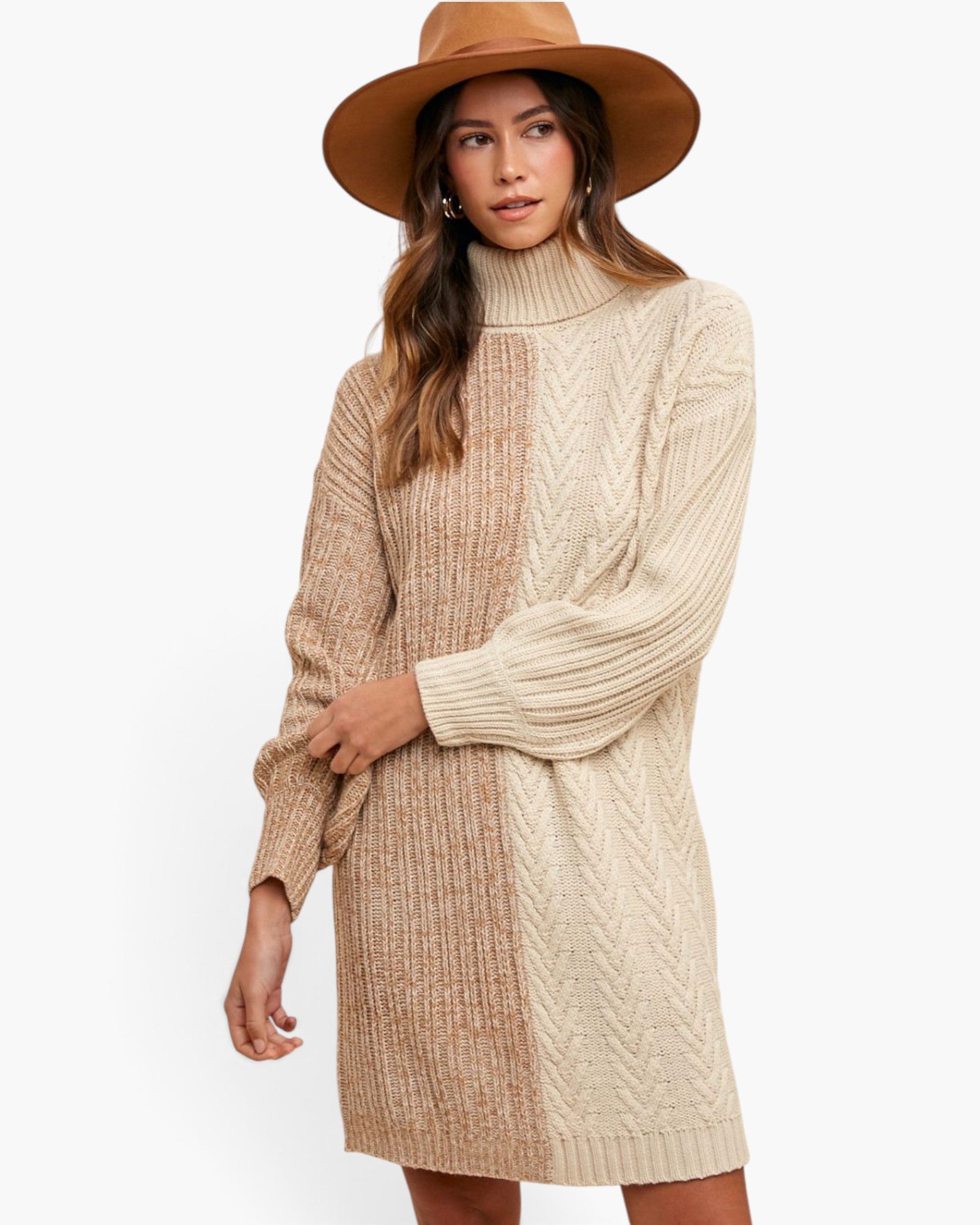 A woman wearing a chunky knit turtleneck sweater dress in a beige and tan color-blocked pattern, styled with a wide-brimmed brown hat against a plain white background.