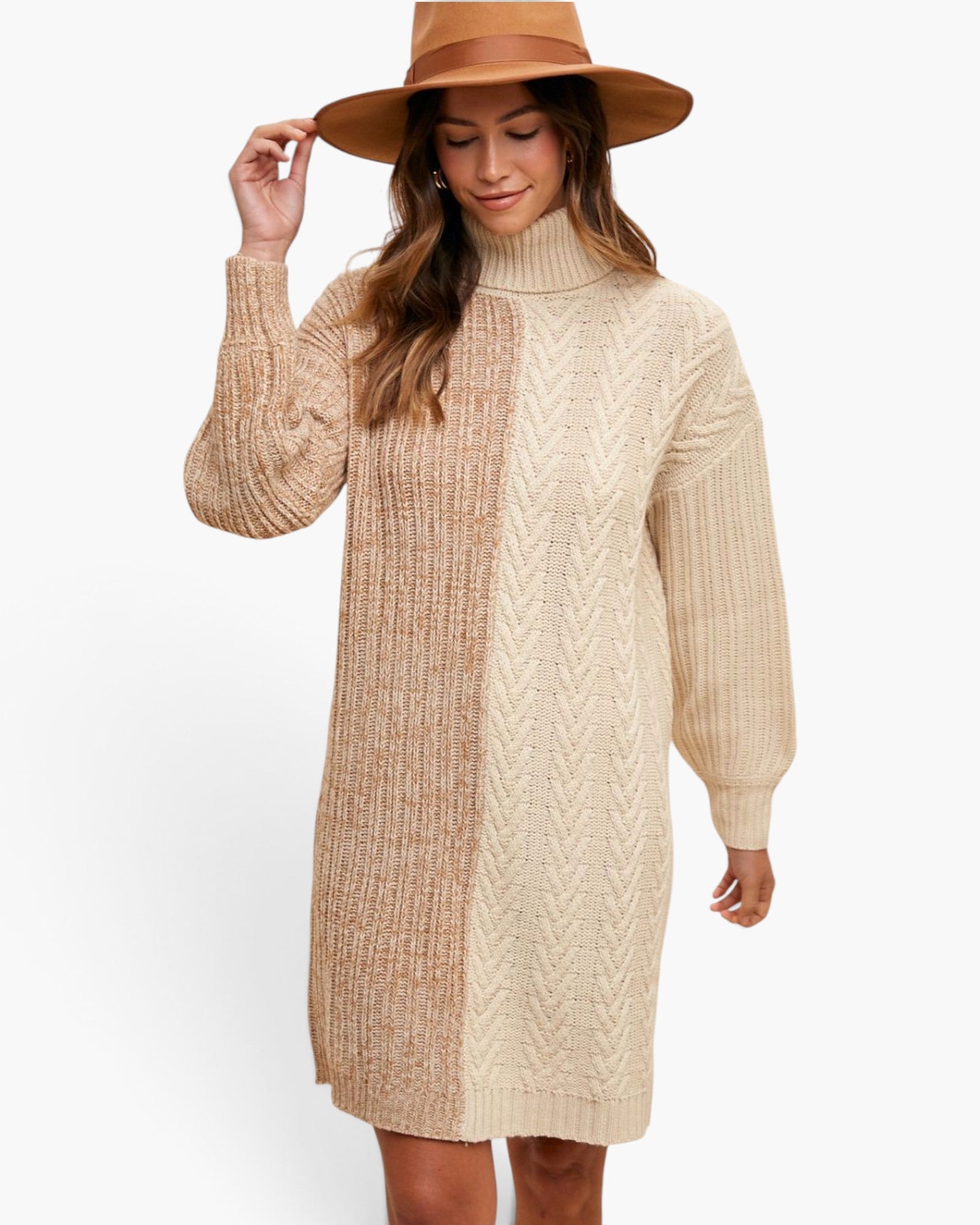 A woman wearing a chunky knit turtleneck sweater dress in beige and cream, styled with a wide-brimmed brown hat, against a plain white background.