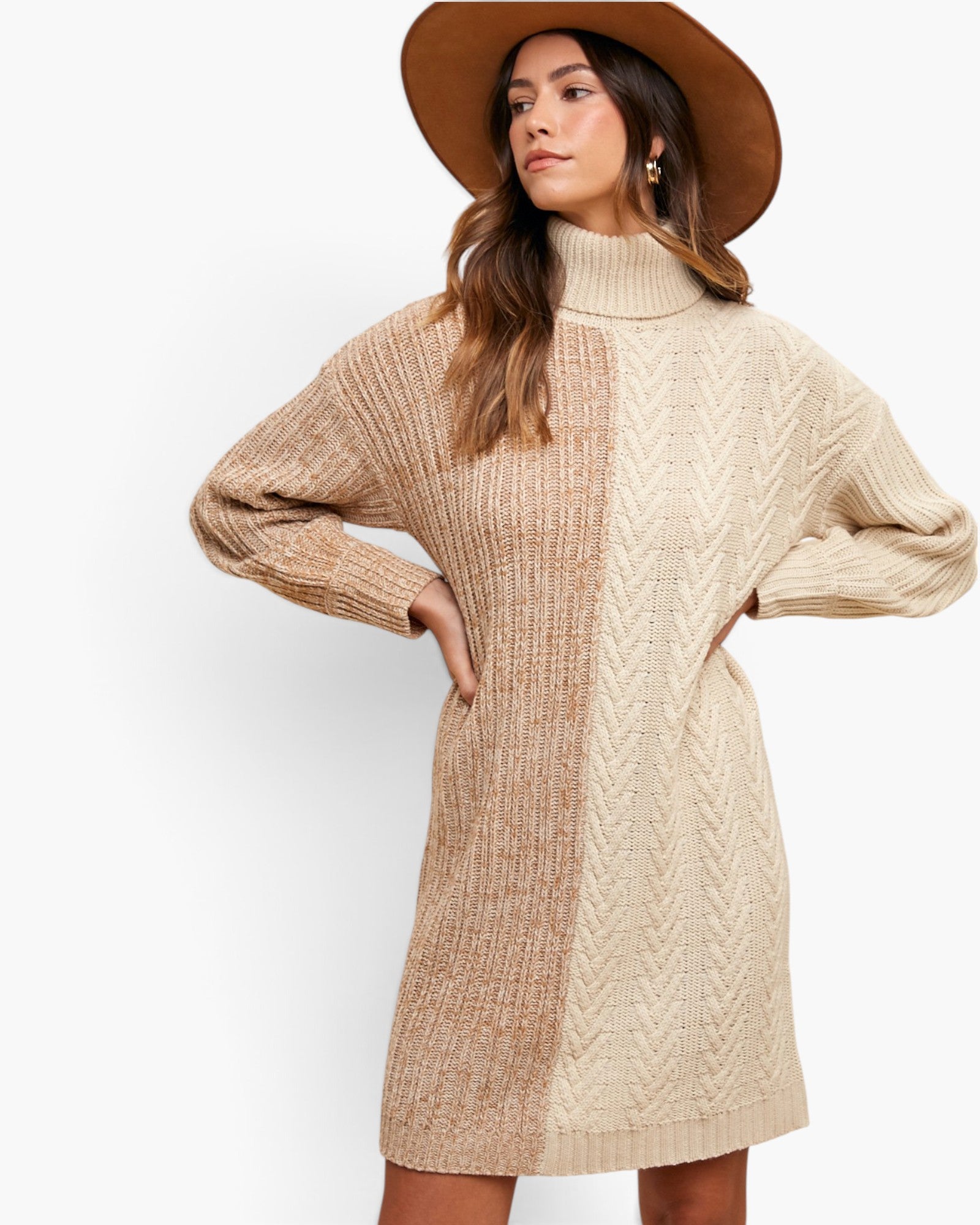 A woman wearing a chunky knit turtleneck sweater dress in beige and tan, styled with a wide-brimmed brown hat, against a plain white studio background.