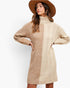 A woman wearing a chunky knit turtleneck sweater dress in beige and tan, styled with a wide-brimmed brown hat, against a plain white studio background.