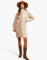 A woman modeling a beige cable-knit turtleneck sweater dress with long sleeves, paired with brown cowboy boots and a wide-brimmed brown hat, against a plain white studio background.