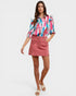 Woman wearing a colorful blouse and pink skirt on a white background