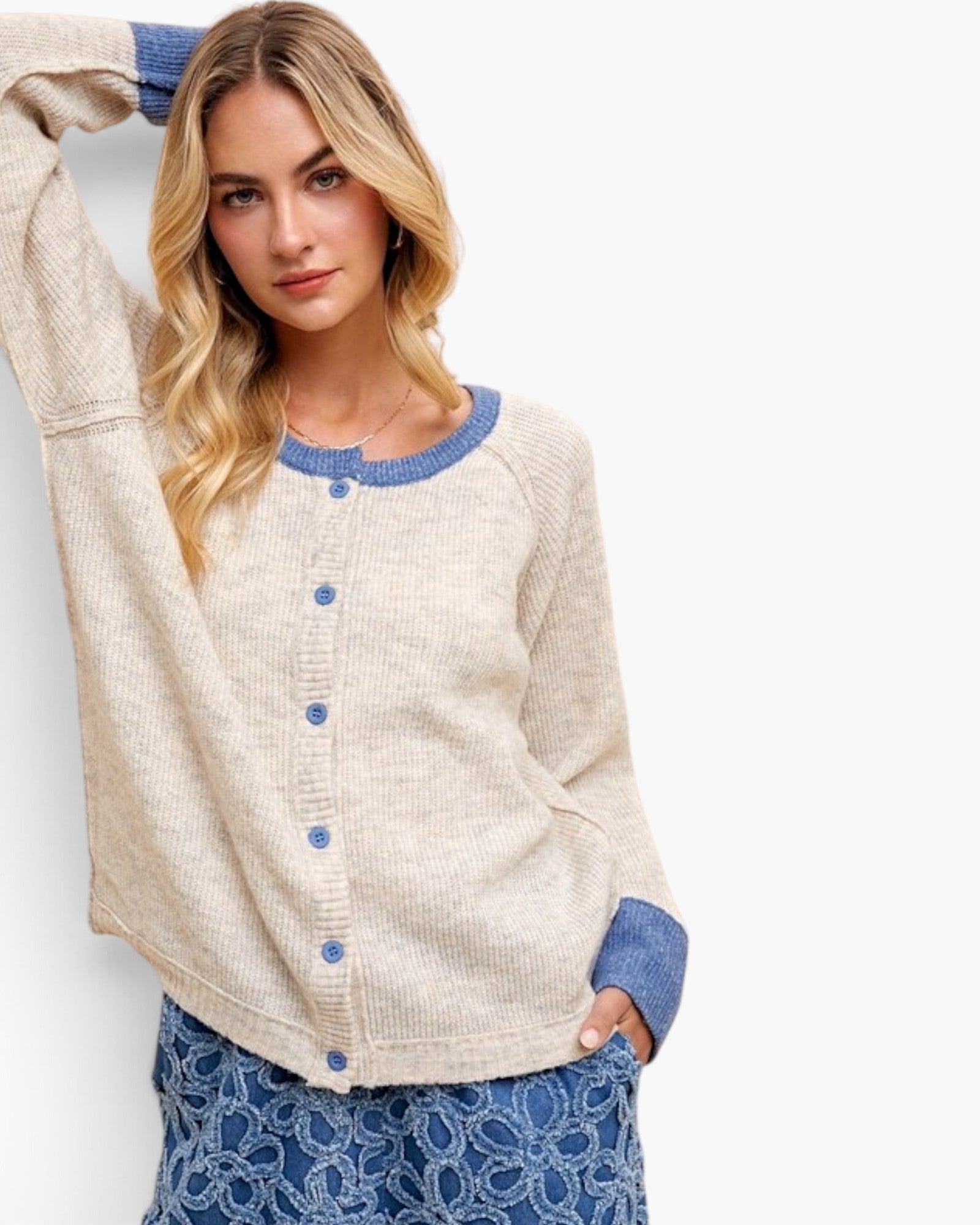 A woman wearing a cream-colored waffle-knit cardigan with blue ribbed trim and blue buttons, paired with a blue patterned skirt, against a plain white background.