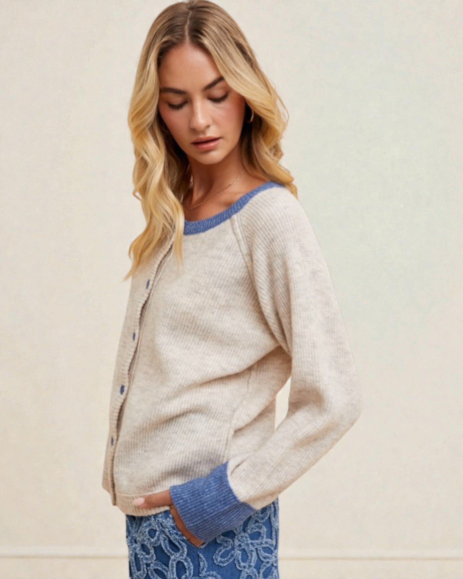 Woman wearing a light gray cardigan with blue trim against a beige background