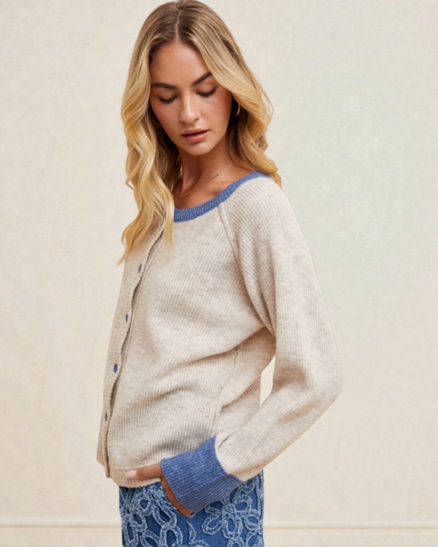 Woman wearing a light gray cardigan with blue trim against a beige background