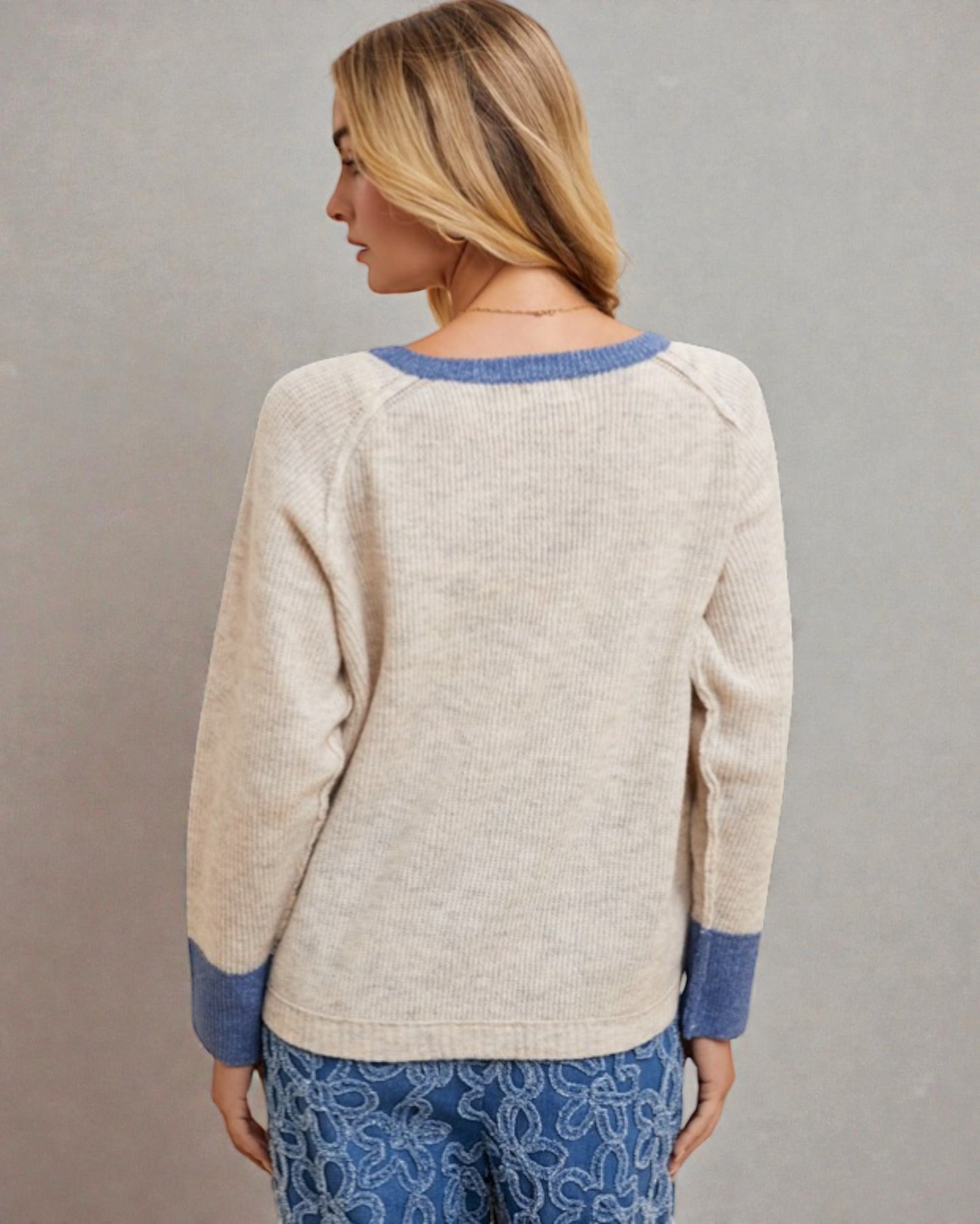 Woman wearing a beige sweater with blue trim against a gray background