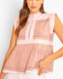 A woman wearing a sleeveless pink peplum top with a mock neck, button placket, and horizontal textured stripe panels, paired with white pants against a light gray studio background.