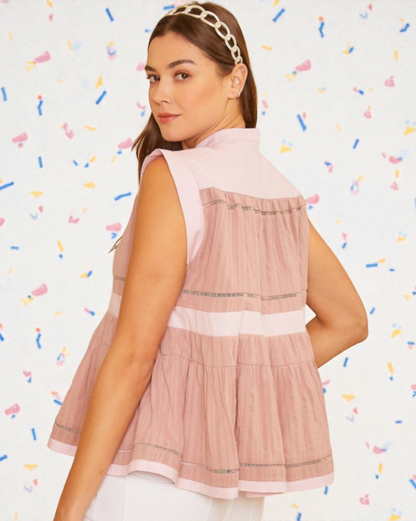 Woman wearing a pink sleeveless top with a white background and colorful confetti-like patterns.