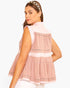 A woman wearing a sleeveless tiered peplum top in light pink and white with thin metallic trim, shown from a three-quarter back view against a plain white background.