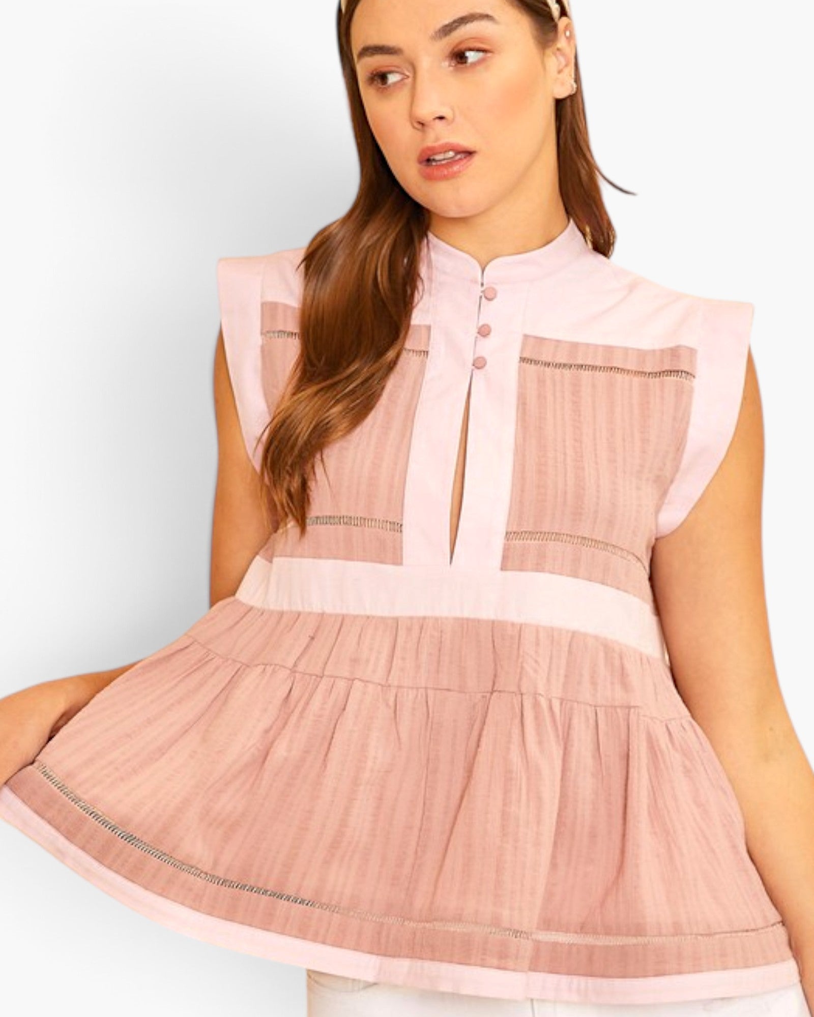 A woman wearing a sleeveless pink peplum-style top with a mock neck, button placket, and gathered skirt, shown against a plain light background.