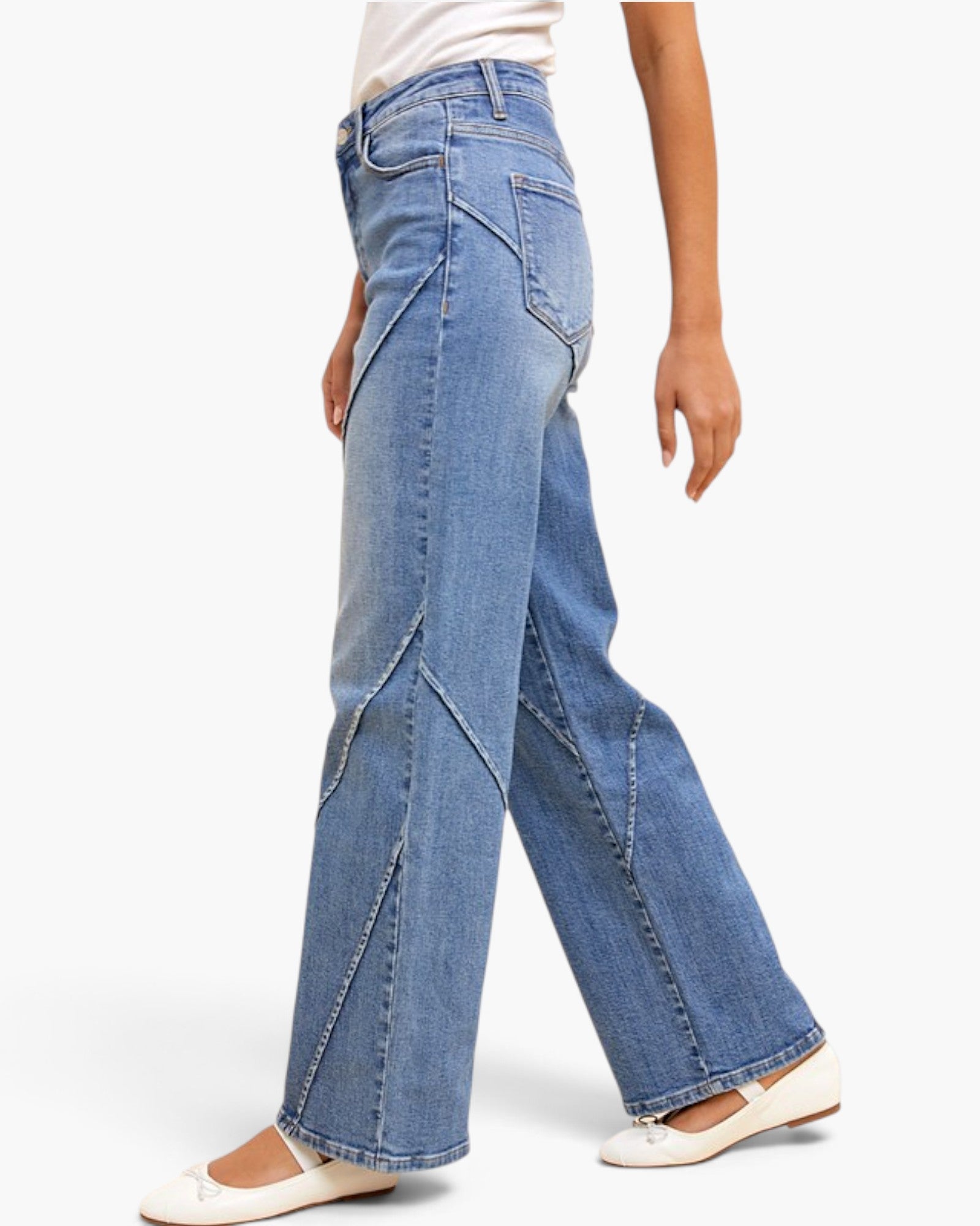 A person wearing light blue wide-leg denim jeans with diagonal seam details, paired with white flats, shown from the waist down against a plain white background.