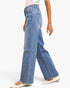 A person wearing light blue wide-leg denim jeans with diagonal seam details, paired with white flats, shown from the waist down against a plain white background.